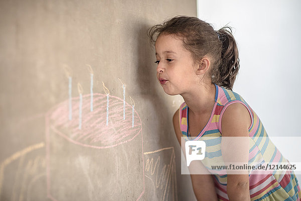 Mädchen  das vorgibt  Kreide auszublasen  Geburtstagskuchen und Kerzenzeichnung auf Betonwand