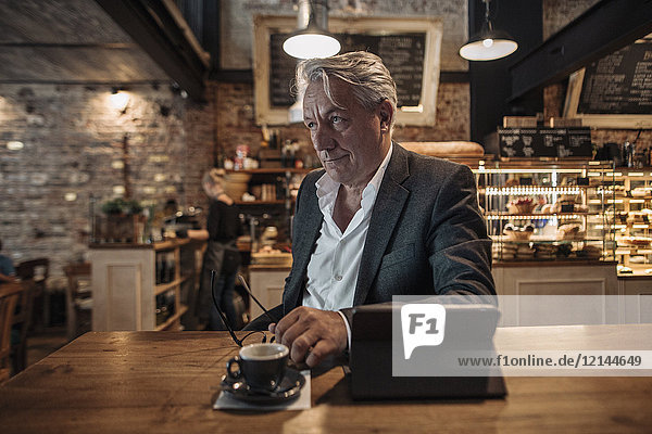 Senior Geschäftsmann sitzend im Cafe  mit digitalen Tabletts  denkend