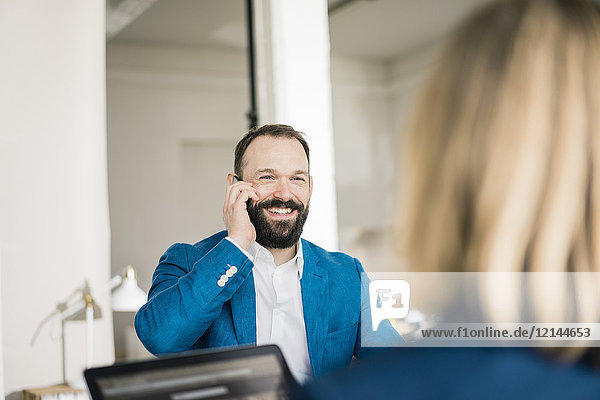 Smiling businessman on cell phone and businesswoman in office
