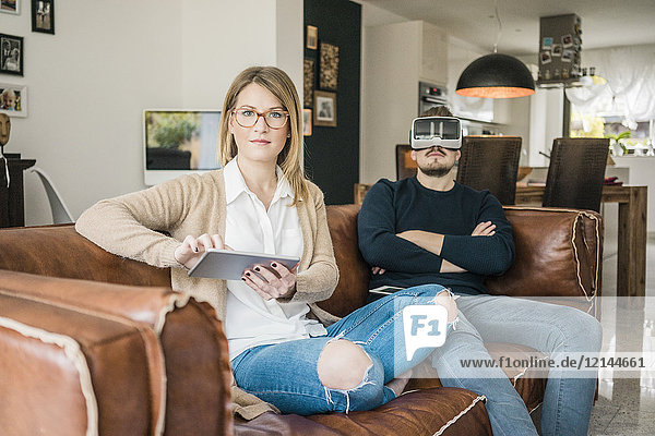 Couple sitting on couch at home with tablet and VR glasses