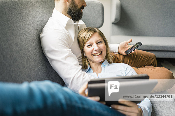 Smiling woman with tablet and man with cell phone on couch