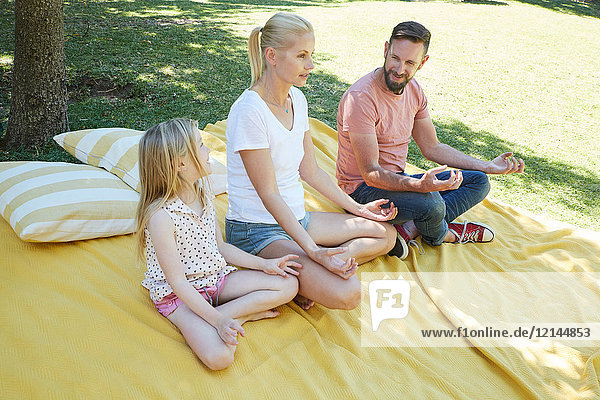 Family with girl practicing yoga on a blanket
