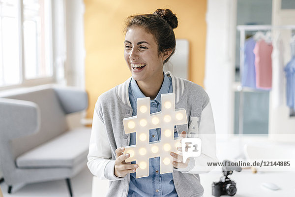 Lachende junge Frau mit Hashtag-Schild im Studio