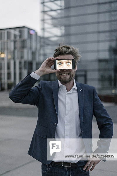 Playful businessman holding cell phone in front of his eyes