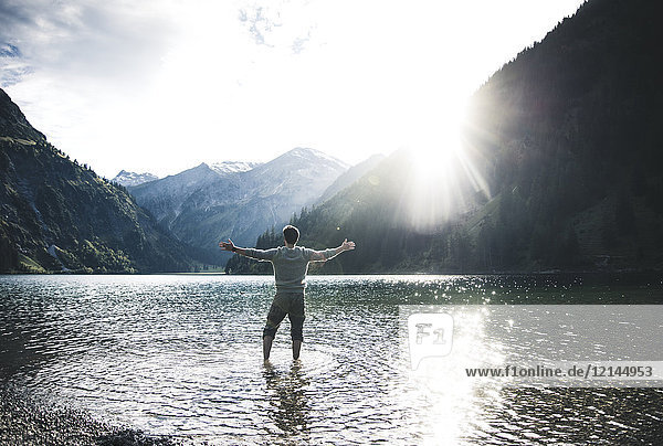 Austria  Tyrol  hiker standing with outstretched arms in mountain lake