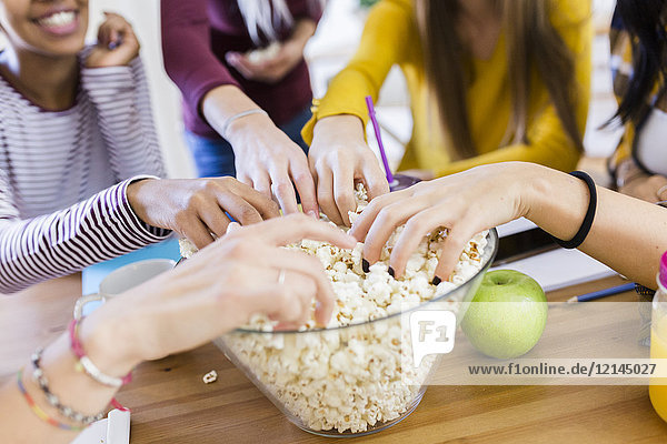 Friends taking popcorn from bowl at table at home