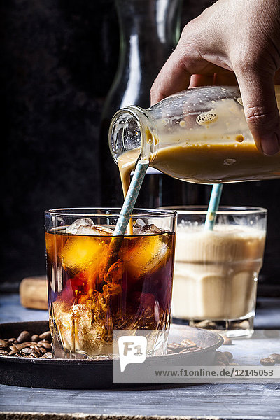 Hausgemachte Kaffeesahne mit Vanillegeschmack von Hand in ein Glas mit Eiskaffee füllen