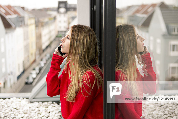 Junge Frau am Fenster in der Stadtwohnung am Handy