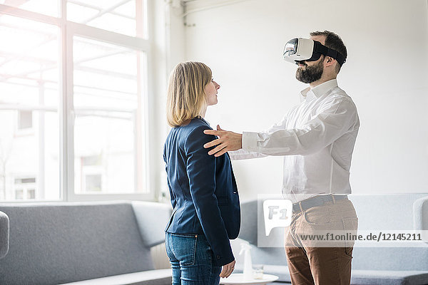 Businessman with VR glasses in office touching businesswoman