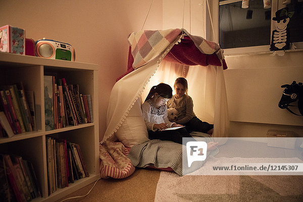 Two girls with dog and tablet in children's room