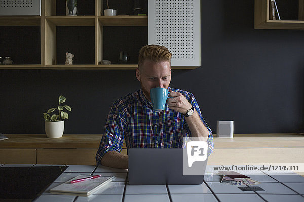 Man drinking coffee and using laptop at home
