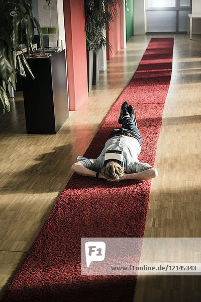 Geschäftsmann auf Teppichboden liegend im Büro mit VR-Brille