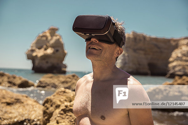 Erwachsener Mann mit VR-Brille zwischen Felsen am Strand