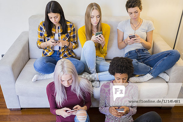 Gruppe von Freundinnen im Wohnzimmer besessen von ihren Smartphones