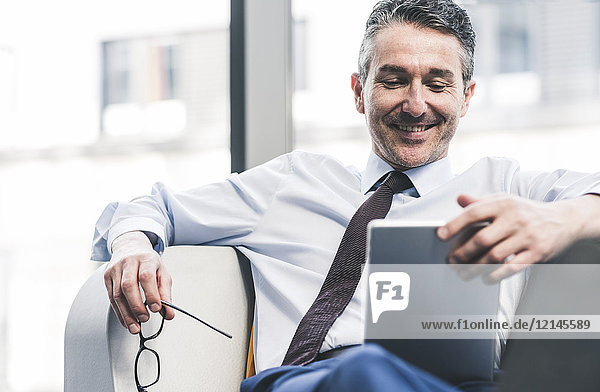 Smiling businessman sitting in lounge with tablet