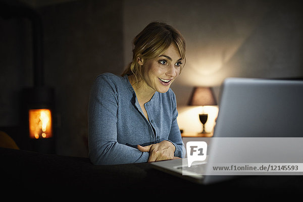 Porträt einer verblüfften Frau  die abends zu Hause mit dem Laptop unterwegs ist.