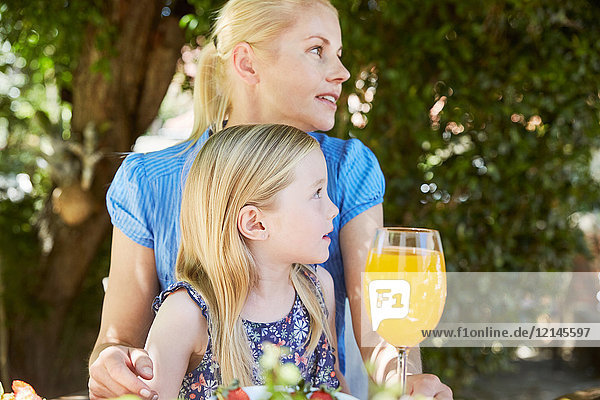 Girl with mother sitting at garden table looking sideways