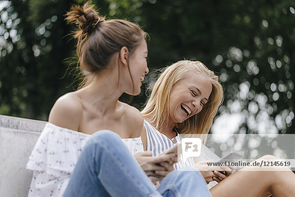 Zwei lachende junge Frauen mit Handys im Freien