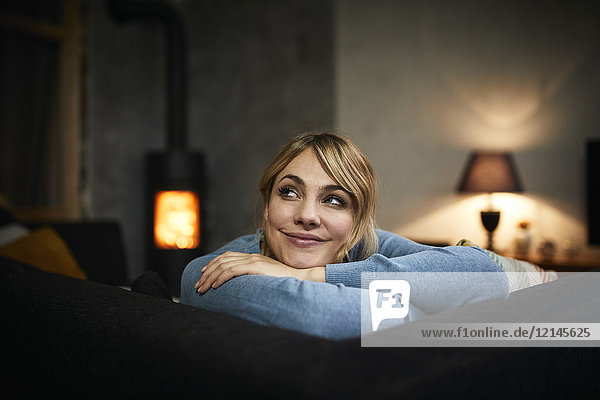 Porträt einer lächelnden Frau  die sich abends zu Hause auf der Couch ausruht