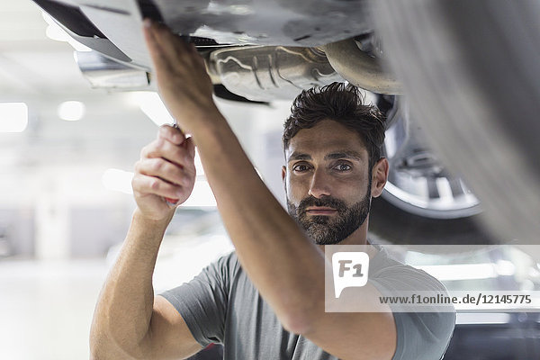 Portrait serious male mechanic working under car in auto repair shop