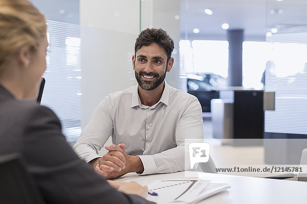 Smiling male customer listening to car saleswoman in car dealership office