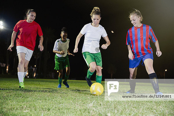 Junge Fußballspielerinnen spielen nachts auf dem Spielfeld und treten den Ball.