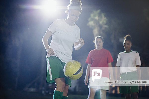 Fokussierte junge Fußballspielerin  die nachts auf dem Spielfeld trainiert und den Ball in die Knie zwingt.