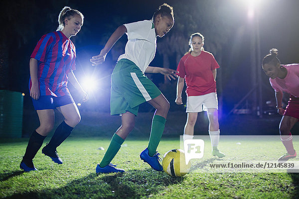 Young female soccer players playing soccer on field at night  kicking the ball