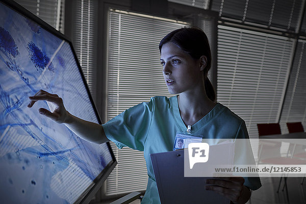 Seriöse Krankenschwester mit Touchscreen-Computermonitor,  Betrachtungsobjektträger