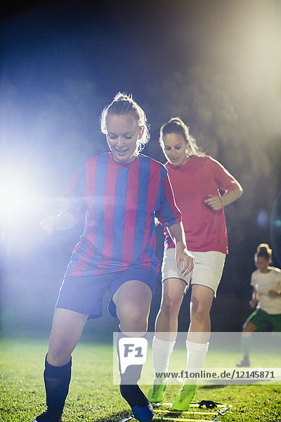 Young female soccer players practicing agility sports drill on field at night