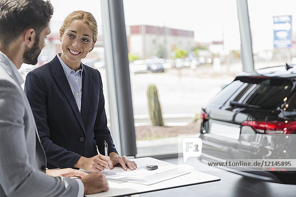 Car saleswoman and male customer signing contract paperwork in car dealership showroom