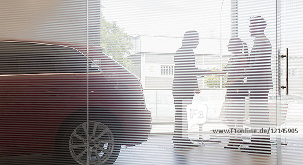 Autoverkäufer beim Händeschütteln mit ein paar Kunden im Autohaus-Showroom