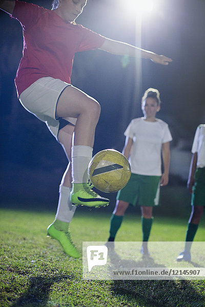 Young female soccer player practicing  jumping and kicking the ball on field at night