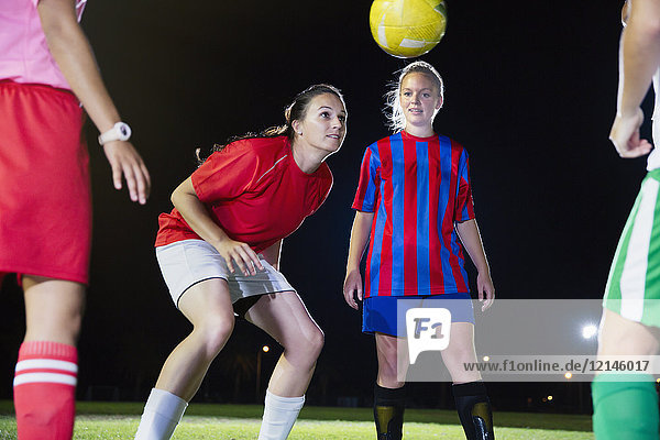 Young female soccer players practicing on field at night  heading the ball