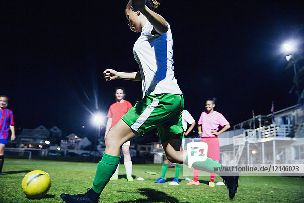 Young female soccer players playing soccer on field at night  kicking the ball