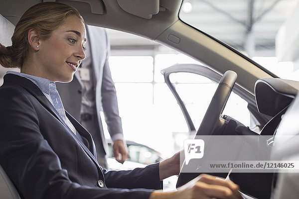 Smiling woman browsing new car  sitting in driver’s seat in car dealership