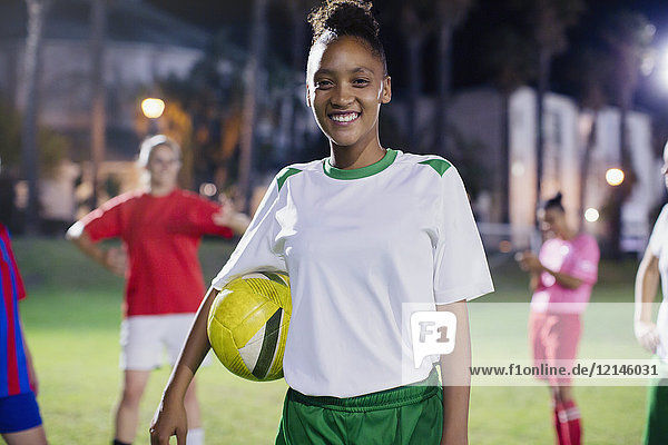 Portrait smiling  confident young female soccer player with ball on field at night