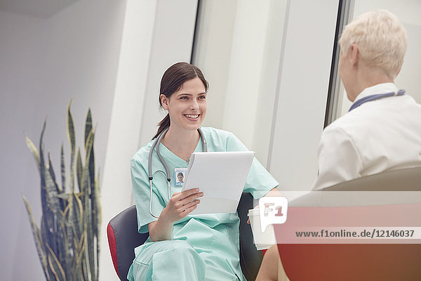 Smiling female nurse with clipboard talking to doctor in hospital