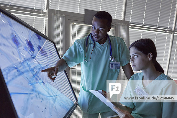 Krankenschwestern mit Zwischenablage zur Untersuchung eines vergrößerten Objektträgers am Computerbildschirm