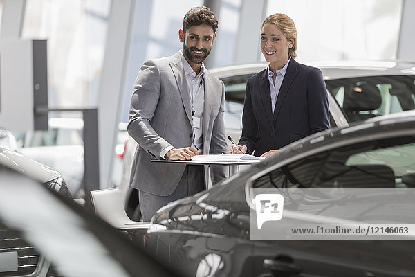 Car salesman and female customer looking at new cars in car dealership showroom