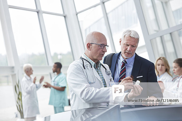Male doctor and pharmaceutical representative discussing medication in hospital lobby