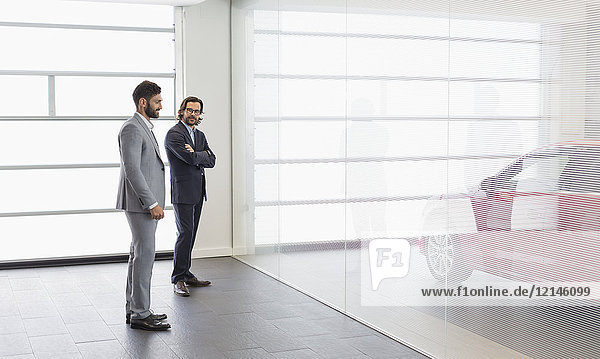 Car salesman and male customer looking at new car in car dealership showroom