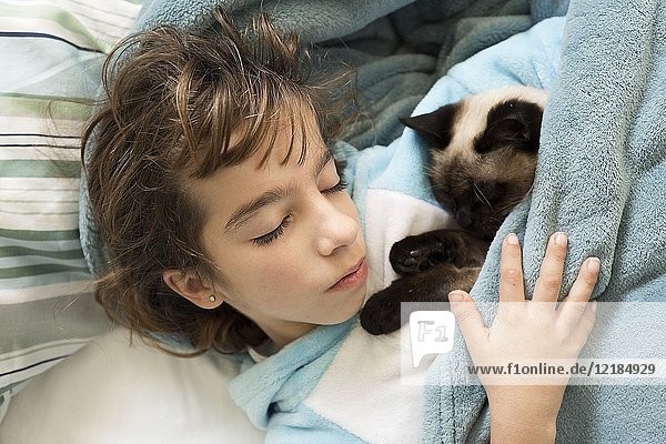 10 year old girl sleeping in bed with her cat on top. Horizontal shot with natural light.