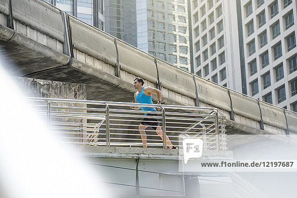 Läufer in blauem Fitness-Shirt über moderne Brücke laufend
