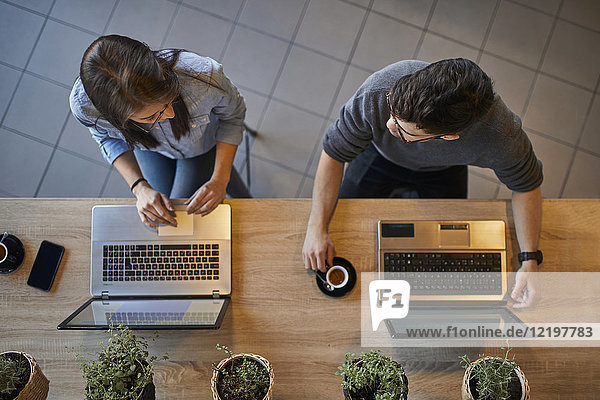 Draufsicht auf junge Frau und Mann in einem Café mit Laptops zur Diskussion