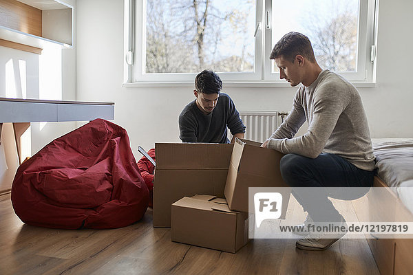 Two young men unpacking cardboard boxes in a room