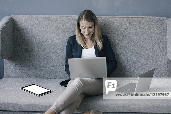 Smiling businesswoman sitting on the couch using laptop