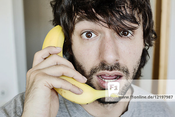 Porträt eines verblüfften jungen Mannes am Telefon mit Banane