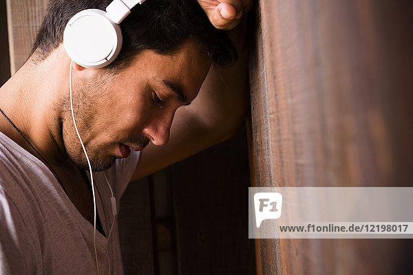 Serious young man wearing headphones leaning against wooden wall