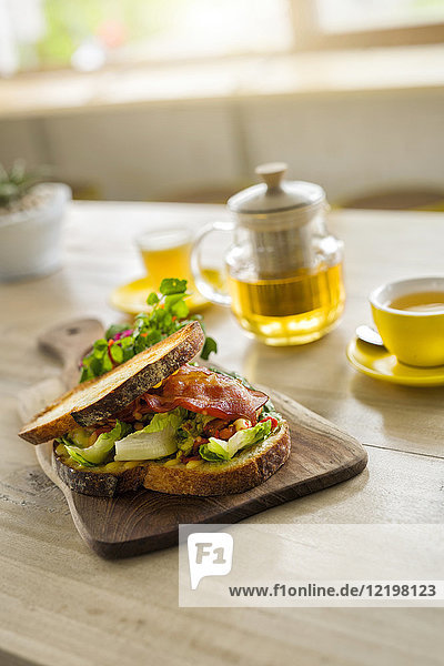 Krustenbrot mit grünem Salat und Schinken auf Holzteller und grünem Tee im Café
